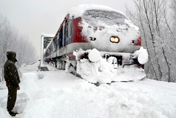 A Railway policeman stands guard as a train runs on snow-covered track at Anantnag Railway Station on Wednesday. —Excelsior/ Sajad Dar