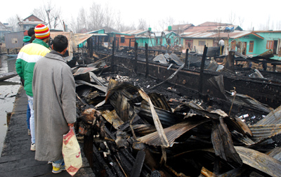 People stand near debris of two Houseboats burnt in Dal Lake in Srinagar on Saturday. —Excelsior/Amin War