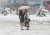 Two women braving snow while moving on road holding umbrella in Baramulla area on Wednesday. —Excelsior/Aabid Nabi
