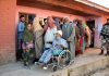 An elderly person returns on a wheel-chair after casting vote as other people wait for their turn to exercise their right to franchise in Shopian on Monday. -Excelsior/Younis Khaliq