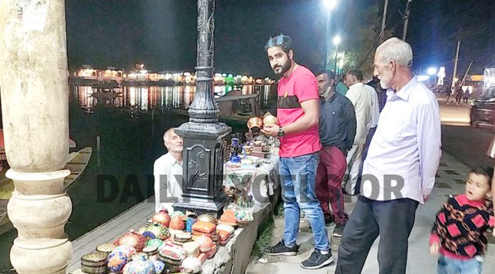 Tourists purchasing famous Kashmiri Paper Mache items from a vendor at Boulevard road on the banks of Dal lake in Srinagar. (UNI)