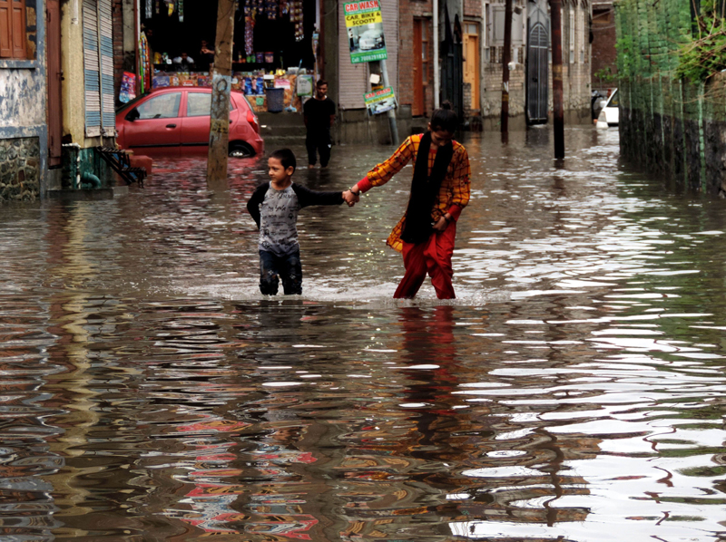 People walking on a waterlogged road in Srinagar after heavy rains on Thursday. (UNI)