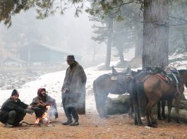 People warm themselves around a bonfire during fresh snowfall in Upper reaches of Kashmir on Monday. (UNI)