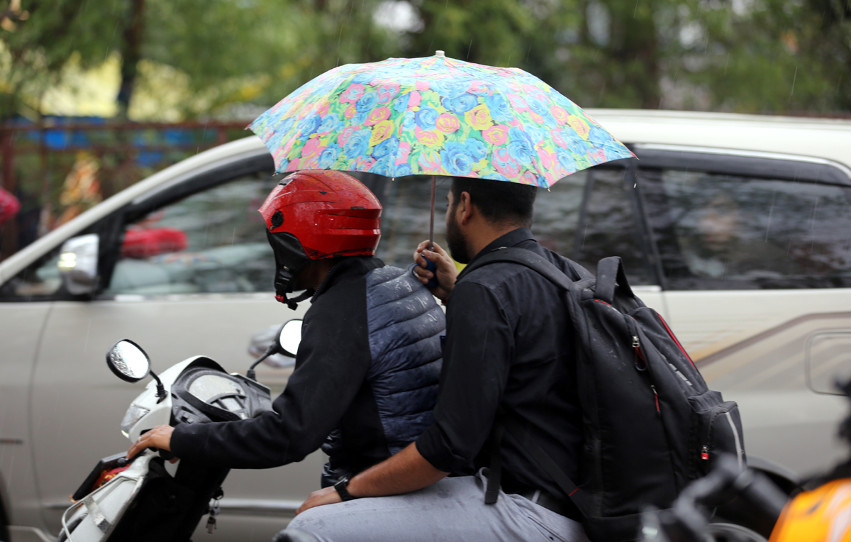 Braving rain, two scooterists taking umbrella cover while moving through a Jammu road on Friday. - Excelsior/Rakesh