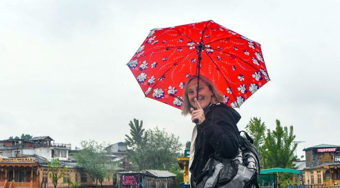 A foreigner tourist takes cover of umbrella during a rain in Srinagar on Tuesday. — Excelsior/Shakeel