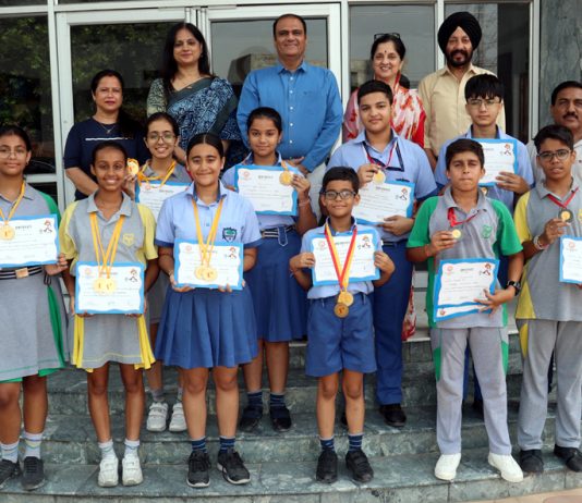 Students displaying medals & certificates while posing with school management.