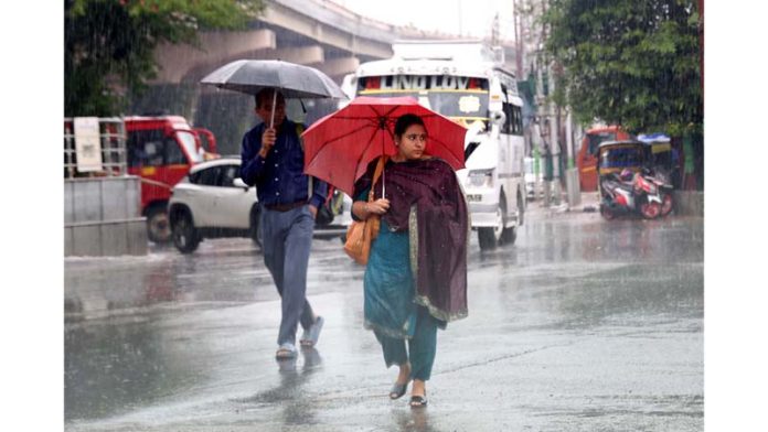 Taking umbrella cover, people move on Jammu roads during rain on Monday. Another pic on page 4. -Excelsior/Rakesh