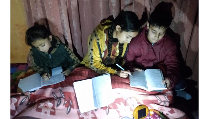 Children reading under the light of a battery operated portable lantern in Bhaderwah. —Excelsior/Tilak Raj.