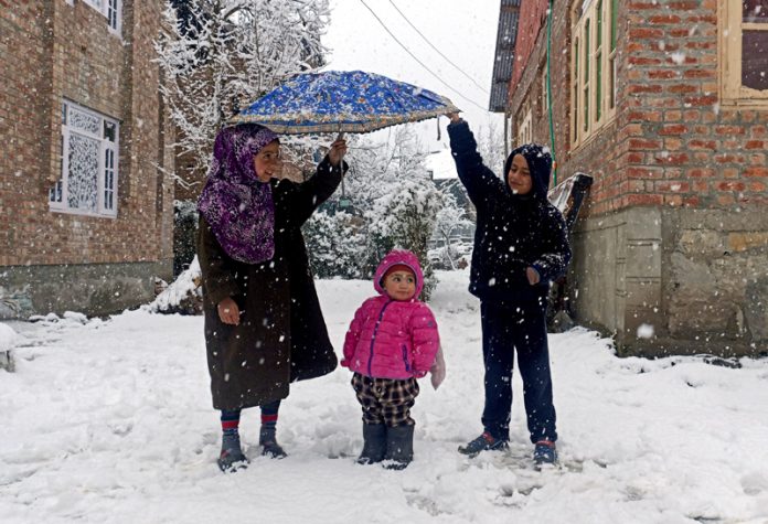 Kids taking cover of umbrella during snowfall in Srinagar on Sunday.