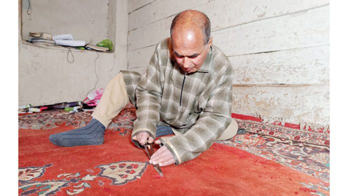 Skilled Rainawari man, an expert in carpet repairing, busy identifying spots that need his attention. —Excelsior/Shakeel