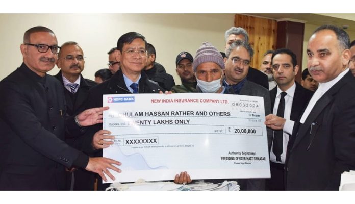 Chief Justice, J&K and Ladakh HC, Justice N Kotiswar Singh along with Justice Tashi Rabstan and others presenting a cheque of compensation to a claimant.
