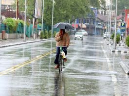 A cyclist takes umbrella cover amid heavy rains in Srinagar on Monday. Excelsior/Shakeel
