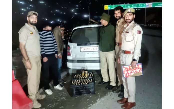 Cops displaying bottles of illicit liquor along with two persons from whom these were recovered in Ramban on Sunday.