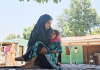 A mother carries her child, suffering from a mysterious disease, in her lap in Panassa village of Reasi district.