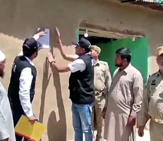 SIA team pasting poster on the house of an absconder in Poonch on Sunday. — Excelsior/Waseem