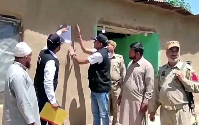 SIA team pasting poster on the house of an absconder in Poonch on Sunday. — Excelsior/Waseem