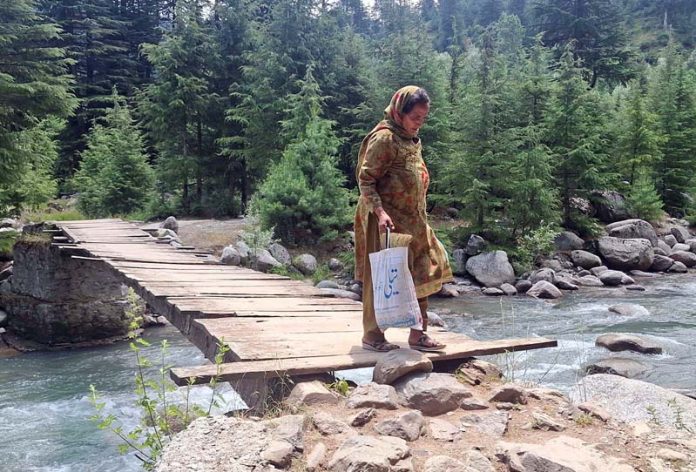 Reshwari Handwara resident crossing the unsafe wooden bridge over Mawar stream on Tuesday. -Excelsior/Aabid Nabi