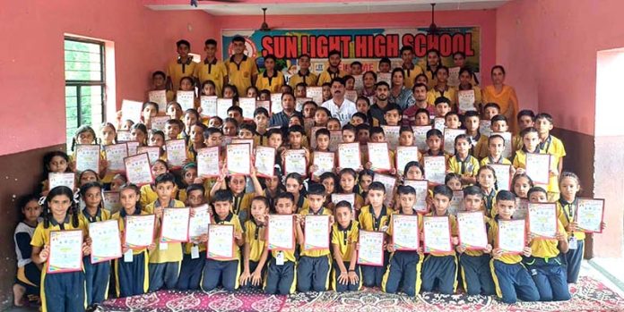 A large group of students displaying certificates while posing during the District Yoga Championship at Samba.