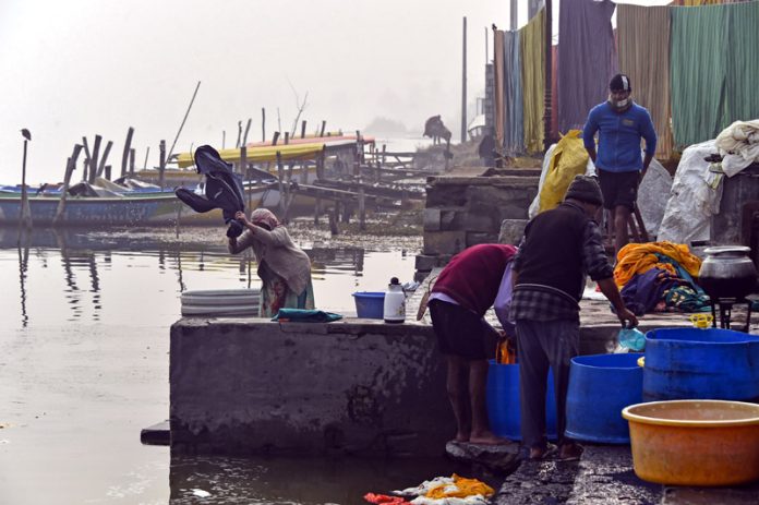 Washermen busy washing clothes along river Jhelum on Friday morning amid bone chilling cold. —Excelsior/Shakeel