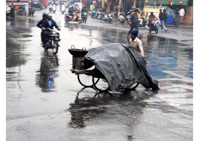 A rehri puller covers eatables and runs through the road amidst rain to seek shelter in Jammu on Monday. -Excelsior/Rakesh