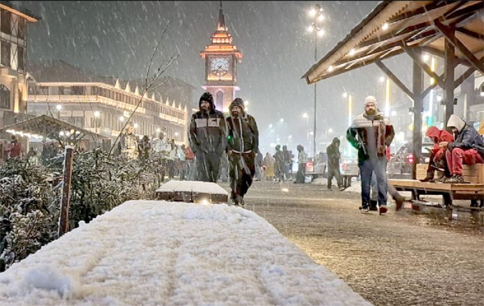 Tourists enjoy fresh snowfall near iconic clock tower, glowing with lights on Sunday evening in Srinagar. -Excelsior/Shakeel